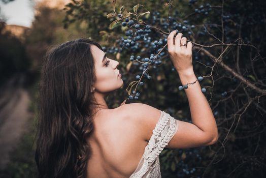 Woman Long-haired bride with bare shoulders near green bush with blueberries in summer