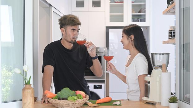 Lovely young couple preparing healthy food and drinking wine at modern home kitchen.