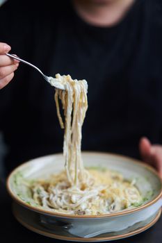 Appetizing carbonara paste with chicken improperly wound on fork. Spaghetti inaccurately hanging and falling from fork. Close up. High quality photo