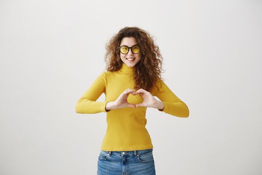 Cheerful beautiful girl making heart by hands isolated on a gray background