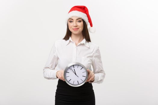 Time management concept - Young happy business woman with santa hat holdinga clock isolated over white background.