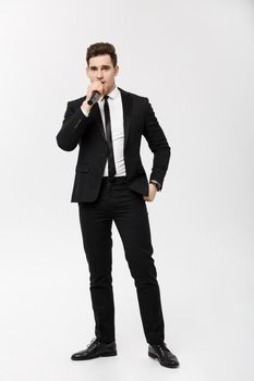 Business Concept: Full-length Portrait young man in black suit is holding a microphone, singing and posing against a white background.