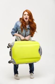 Travel and Lifestyle Concept: Young woman suffers from back pain lifting a heavy suitcase isolated on yellow background.