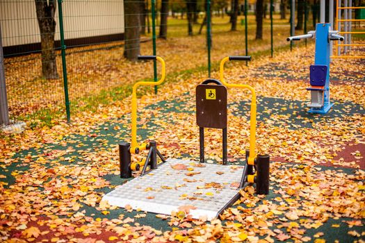 Disabled simulator in the autumn park. Yellow autumn leaves lie on the playground. Physiotherapeutic rehabilitation simulator on the street in a city park. Patient recovery.