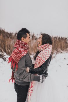 young man and woman running lying in the snow laughing fooling around having fun playing snowballs.bride and groom in love couple in knitted scarf and mittens in winter and snowflakes. mexican people