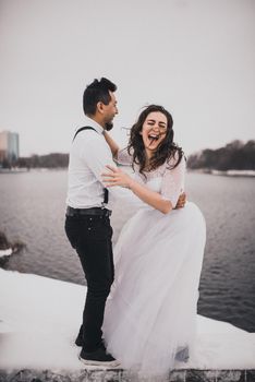 Mexican Hispanic man in suspenders and woman are kissing hugging laughing. groom and bride wedding love couple in winter in snow. fashionable stylish party wedding wear 2021