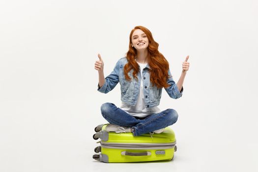 Traveling and Lifestyle concept. Young excited caucasian woman sitting on the luggage valise showing thumb up. Isolated on white. Ready for vacation