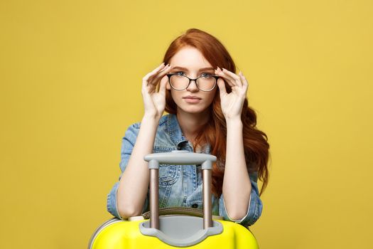 Travel and Lifestyle Concept: Portrait of a shocked girl in denim dress with suitcase looking at camera isolated over golden yellow background.