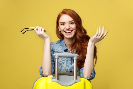 Travel Concept: Happy tourist woman wearing jean clothes ready for travel with suitcase and passport. Isolated over bright yellow background
