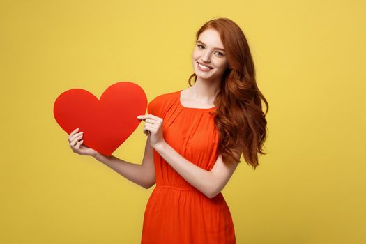 Lifestyle and Holiday Concept - Portrait Young happy red hair woman in orange beautiful dress holding big red heart paper