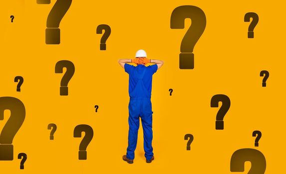 Rear view of a male builder in a helmet with his hands on his head, standing in front of a wall with many questions, was left without work in the conditions of the economic crisis