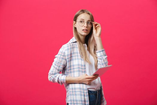 young business woman holding tablet and thinks on pink backgrouond.