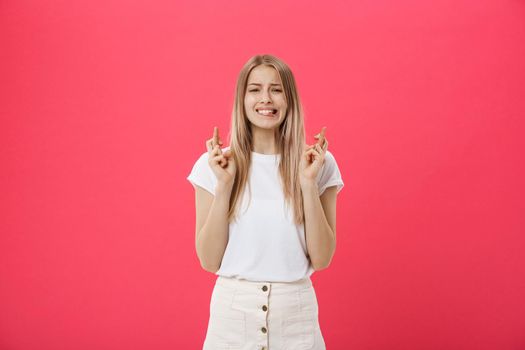 Portrait of a smiling casual girl holding fingers crossed for good luck isolated over pink background.