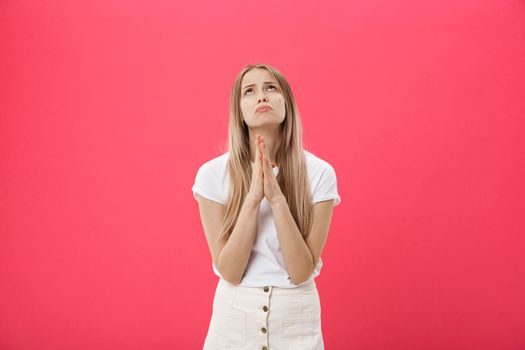 Close up portrait of beautiful Caucasian teenage girl praying isolated against pink background. Student girl with red hair and healthy freckled skin, holding hands in prayer, hoping for the best.