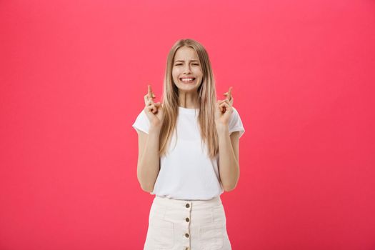 Portrait of a smiling casual girl holding fingers crossed for good luck isolated over pink background.