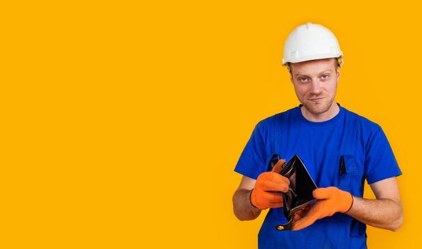 The puzzled worker in overalls holds his empty purse without money. The concept of economic crisis, unemployment and production, coronavirus, pandemic, health.