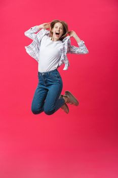 Full length portrait of a crazy joyful girl in casual cloth while jumping isolated over pink background.