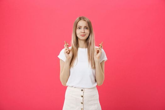 Portrait of a smiling casual girl holding fingers crossed for good luck isolated over pink background.
