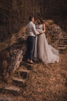 married couple a man with a pregnant woman with a big belly in nature near the mountain are walking on stone steps