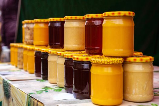 Natural honey in glass jars on the market. Jars with various kinds of pure, raw, fresh honey. Glass jars with different varieties of honey.