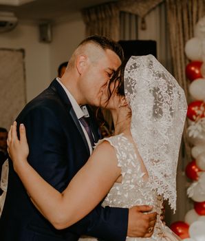 groom and bride already with their heads covered shawl hustka hug kissing dancing at the end of the wedding. Slavic Ukrainian Russian traditions