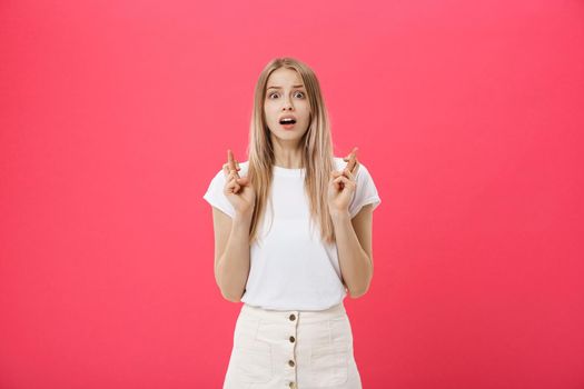 Portrait of a smiling casual girl holding fingers crossed for good luck isolated over pink background.