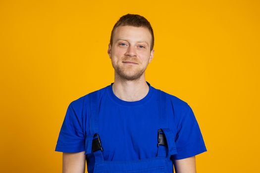Portrait of a male worker in overalls. Red-haired young technician on a yellow background.