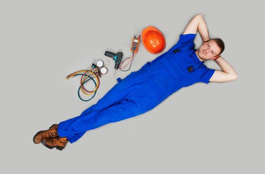 The male builder was left without work in the economic crisis. Unemployment is no job. A male worker lies on his back, next to a string instrument on a gray background