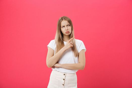 portrait of attractive young girl with sad and disappointed expression, pointing index fingers in both sides, isolated over pink background. Woman confused, don't know what to do