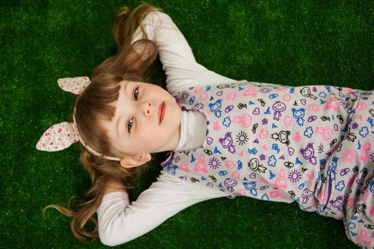 Beautiful girl lying on the green grass and looking up. Girl on a green background top view. Childhood concept.