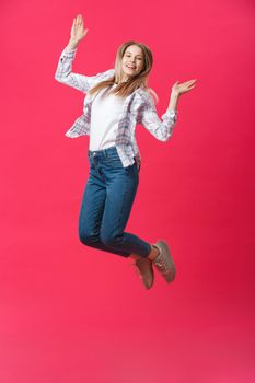 Full length portrait of a crazy joyful girl in casual cloth while jumping isolated over pink background.