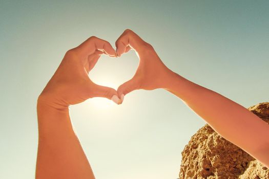Female hands in the form of heart against the sky pass sun beams. Hands in shape of love heart