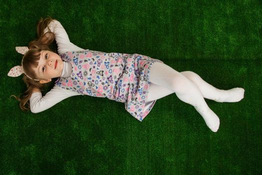 Beautiful girl lying on the green grass and looking up. Girl on a green background top view. Childhood concept.