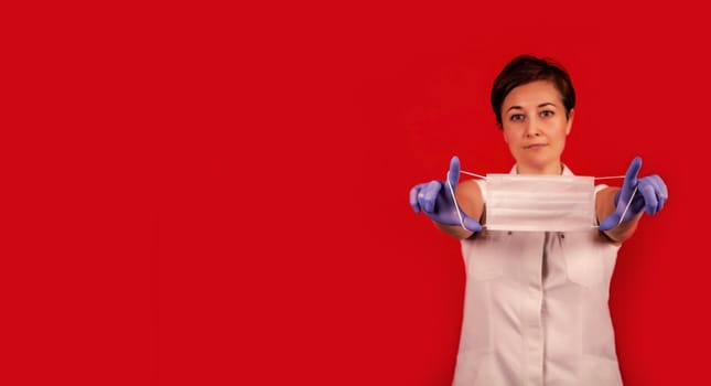 Female hands hold a medical mask. Young professional doctor woman holds a medical mask in her hands. Virus Protection Group. Red danger background