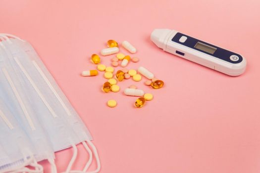 Medical disposable masks, pills and electronic thermometer on a pink background. Protection against influenza virus and pneumonia. Healthcare and medical concept.