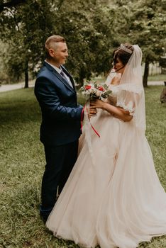 blonde European Caucasian young man groom in blue suit and black-haired woman bride in white wedding dress with long veil and tiara on head. first meeting newlyweds groom wait sees bride hug