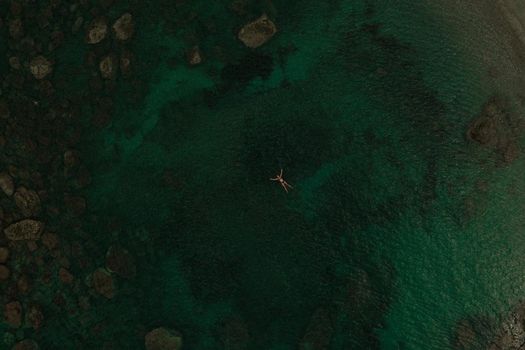 Aerial top nature view above green turquoise Adriatic sea in Albania. Beautiful young woman swimming alone in middle ocean water. girl in swimsuit bikini lying. wide panoramic view marine. summer