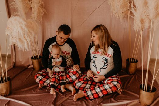family photo in studio on beige background with flowers dry reeds. clothes for baby child.pregnant woman in pajamas.Christmas morning.New Year interior.Valentine's day celebration