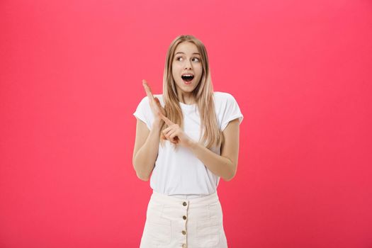 Cute young woman wearing white t-shirt points a finger away isolated over pink background.