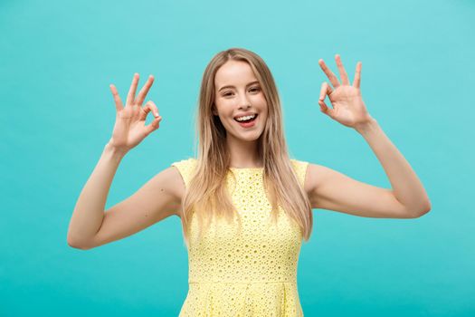 Happy young woman showing ok sign with fingers with big smile isolated on a blue background.