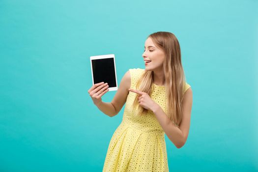 Happy attractive caucasian woman pointing finger on tablet at copy space isolated over blue background.