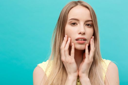 Beauty Concept: Portrait of beauty model with natural nude make up and touching her face. Spa, skincare and wellness. Close up, blue background, copyspace