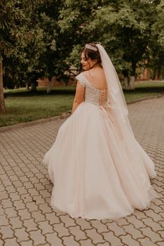 dark-haired European Caucasian young woman bride in white wedding dress with long veil and tiara on head spinning whirls dancing posing moving at nature on background greenery. Valentine love couple