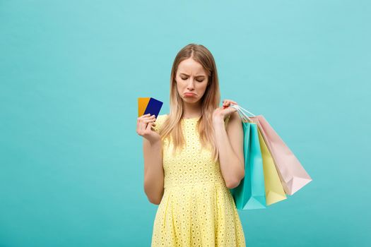 Portrait of a sad woman holding shopping bags and bank card isolated on a blue background.