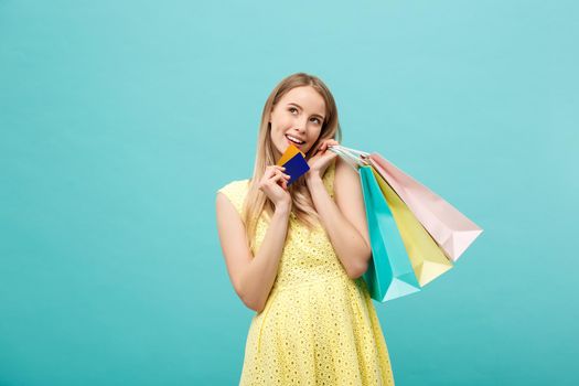 Shopping and Lifestyle Concept: Beautiful young girl with credit card and colorful shopping bags. Isolated on blue background.