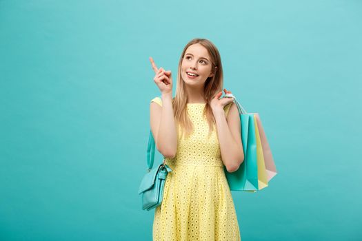 Beautiful young girl with shopping bag in yellow dress points to something with her finger