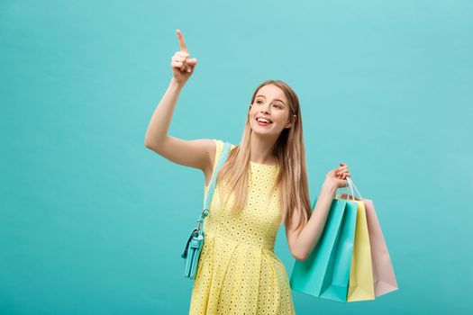 happy shopping young woman finger point to copy space with bags - isolated on blue background