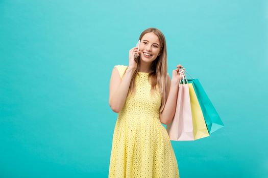 Portrait of happy fashion caucasian woman with shopping bags calling on mobile phone. Isolated on blue background