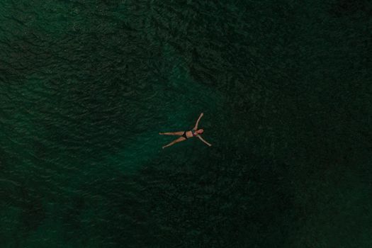 Aerial top nature view above green turquoise Adriatic sea in Albania. Beautiful young woman swimming alone in middle ocean water. girl in swimsuit bikini lying. wide panoramic view marine. summer