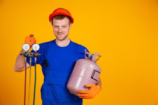 Young cheerful smiling air conditioning specialist. Repair of air conditioners and manometers, measuring equipment for refueling air conditioners. On a yellow background